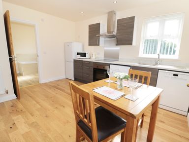A kitchen with wooden floor wooden dining table and chairs next to window and cabinets at Breamish in Longframlington
