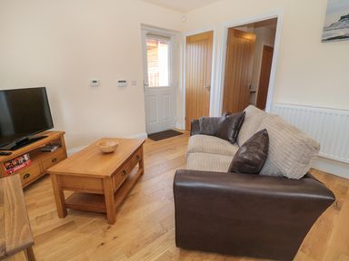 A living room with a brown and beige sofa wooden coffee table wooden tv stand and a television at Breamish in Longframlington