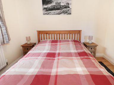 A bedroom with a wooden bed frame and red plaid bedspread with two bedside tables and lamps at Breamish in Longframlington