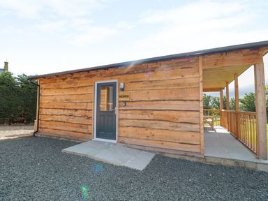 An exterior view of a wooden cabin with a gray door and a covered porch at Breamish in Longframlington