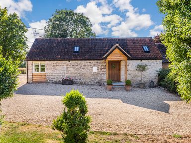 A stone house with a tiled roof and a wooden door surrounded by gravel and plants at Old Farm Stables South Barrow near Sparkford