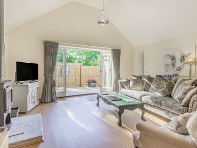 A living room with a sofa an armchair a coffee table a television and glass doors opening to a fenced garden at Old Farm Stables South Barrow near Sparkford
