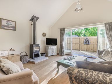 A living room with sofas a coffee table a wood stove TV and large sliding doors at Old Farm Stables South Barrow near Sparkford