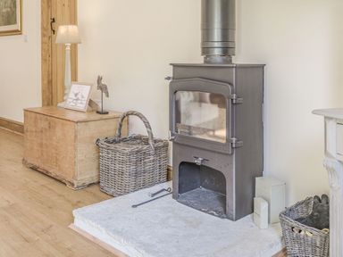 A wood-burning stove with baskets and a wooden chest with a lamp and decorations beside it at Old Farm Stables South Barrow near Sparkford