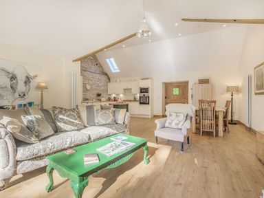 An open plan living space with a patterned sofa, green coffee table, armchair, dining table with chairs and kitchen area at Old Farm Stables South Barrow near Sparkford