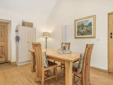A dining room with a wooden table and four chairs a lamp a cabinet and a framed picture on the wall at Old Farm Stables South Barrow near Sparkford