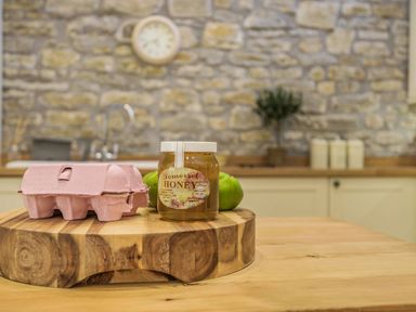 A jar of honey and a pink egg carton on a wooden cutting board in a kitchen at Old Farm Stables South Barrow near Sparkford