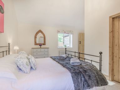 A bedroom with a bed with floral pillows and a gray blanket a dresser with a mirror and flowers and a window at Old Farm Stables South Barrow near Sparkford