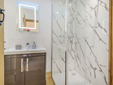 A bathroom with a sink and cabinet next to a glass shower enclosure with marble patterned walls at Old Farm Stables South Barrow near Sparkford
