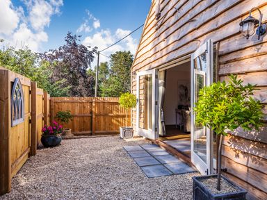 An outdoor patio area with gravel ground a wooden fence and potted plants next to open glass doors of a wooden building at Old Farm Stables South Barrow near Sparkford