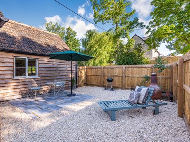 A backyard with a wooden fence a table with two chairs and an umbrella and a lounge chair at Old Farm Stables South Barrow near Sparkford