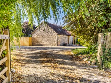 A stone house with a tiled roof surrounded by trees and a gravel driveway at Old Farm Stables South Barrow near Sparkford