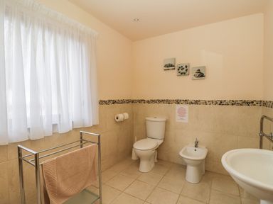 A bathroom with a toilet bidet sink towel rack and window with curtains at Burnside Lodge (Lodge 1 Glengoulandie) in Aberfeldy