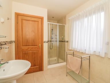A bathroom with a wooden door a shower with glass doors a sink a towel rack and a window with white curtains at Burnside Lodge in Aberfeldy