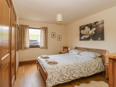 A bedroom with a double bed wooden furniture window with curtains and floral bedding at Burnside Lodge in Aberfeldy