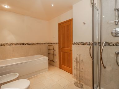 A bathroom with a bathtub a toilet a bidet a wooden door a shower with glass doors and a metal rack at Burnside Lodge (Lodge 1 Glengoulandie) in Aberfeldy