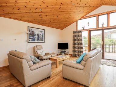 A living room with beige sofas a wooden coffee table a tv and wooden ceiling at Burnside Lodge in Aberfeldy