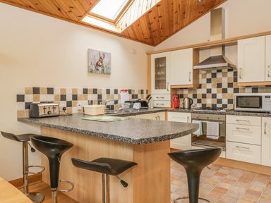 A kitchen with black stools at a counter a toaster kettle microwave and oven with a tiled backsplash at Burnside Lodge in Aberfeldy
