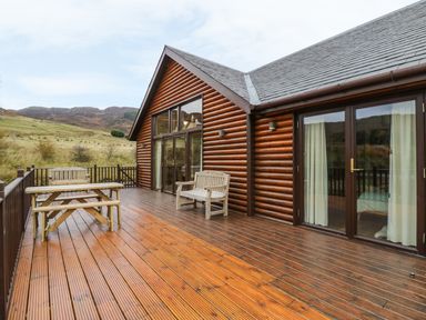 A wooden deck with benches and a picnic table outside a log cabin at Burnside Lodge in Aberfeldy