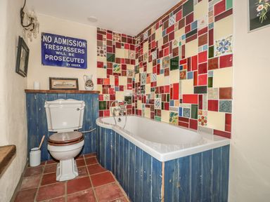 A bathroom with a bathtub and toilet with blue wooden paneling and colorful tile wall at Jackdaw's Roost in Cheltenham