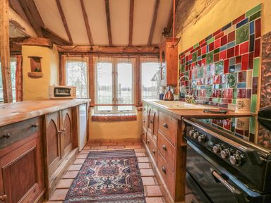 A kitchen with wooden cabinets a tiled backsplash a microwave and a patterned rug at Jackdaw's Roost in Cheltenham