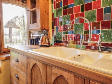 A kitchen sink with a dual basin and chrome faucet on a wooden countertop with colorful tiled backsplash at Jackdaw's Roost in Cheltenham