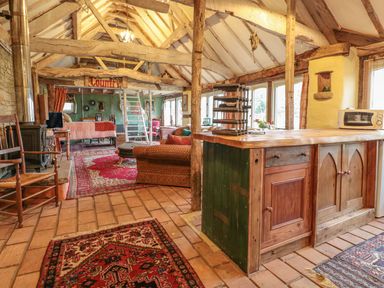 A rustic open living area with exposed beams rugs a wood stove and a kitchen island at Jackdaw's Roost in Cheltenham