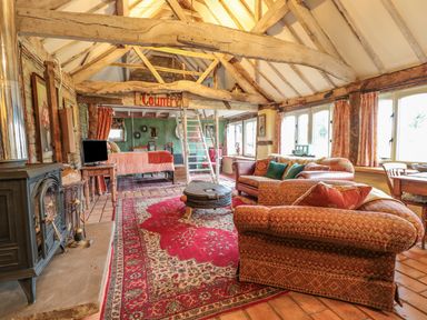 A living area with sofas a wood stove a bed and wooden beams at Jackdaw's Roost in Cheltenham