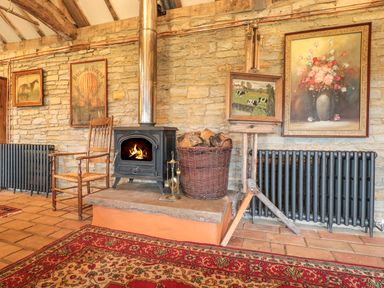 A room with a wood-burning stove a wooden chair paintings on stone walls and a red patterned rug at Jackdaw's Roost in Cheltenham