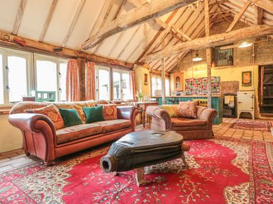 A living room with wooden beams a sofa armchair and a coffee table on a red rug at Jackdaw's Roost in Cheltenham