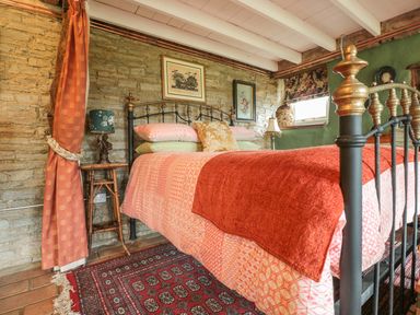 A bedroom with a metal bed frame a red blanket a patterned rug and a stone wall at Jackdaw's Roost in Cheltenham