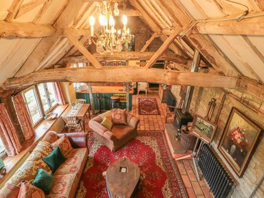 A living room with wooden beams and a chandelier featuring sofas rugs and a wood stove at Jackdaw's Roost in Cheltenham