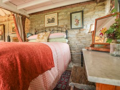 A bedroom with a bed covered in blankets and pillows next to a dresser with a mirror and flowers at Jackdaw's Roost in Cheltenham