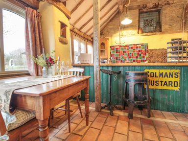 A rustic kitchen with a wooden table set with glasses and a flower vase and a green bar counter with stools at Jackdaw's Roost in Cheltenham