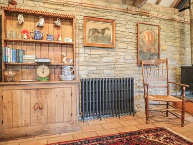 A rustic room with a wooden cabinet holding teapots cups books and a scale next to a radiator and wooden chair at Jackdaw's Roost in Cheltenham