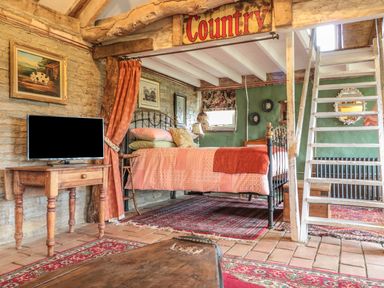 A bedroom with a metal bed frame a wooden table with a TV and a staircase in a country style room at Jackdaw's Roost in Cheltenham