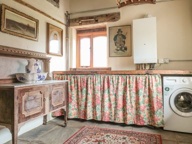 A utility room with a washing machine floral curtain under the counter wooden cabinet and framed pictures on the wall at Jackdaw's Roost in Cheltenham