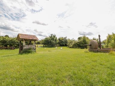 An outdoor green grassy area with a wooden well structure and stone mill wheel with birds in the middle at Jackdaw's Roost in Cheltenham