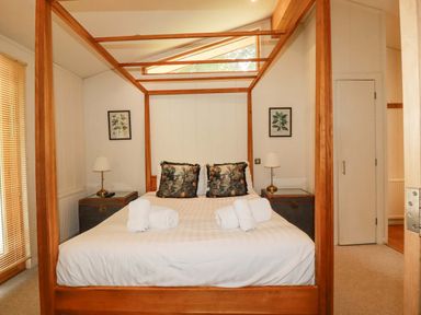 A bedroom with a wooden four poster bed two bedside tables with lamps and framed pictures on walls at 4 Stonerush Valley in Lanreath
