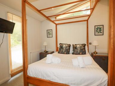 A bedroom with a four poster bed two bedside tables with lamps a wall mounted television and framed pictures at 4 Stonerush Valley in Lanreath