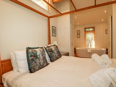 A bedroom with a wooden bed frame and pillows and a bathtub visible in an adjacent room at 4 Stonerush Valley in Lanreath