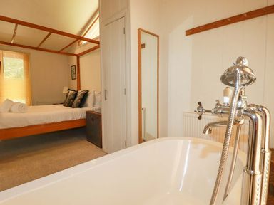 A bedroom with a four-poster bed and a freestanding bathtub with a showerhead at 4 Stonerush Valley in Lanreath