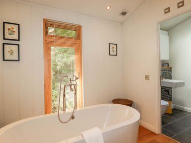 A bathroom with a freestanding bathtub white walls framed flower pictures and an adjoining room with a sink and toilet at 4 Stonerush Valley in Lanreath