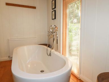 A bathroom with a white freestanding bathtub a radiator wooden floor and a window with blinds at 4 Stonerush Valley Lanreath