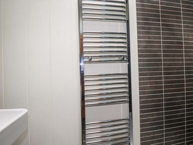 A chrome towel rail mounted on a white wall next to a wall with brown rectangular tiles in a bathroom at 4 Stonerush Valley in Lanreath