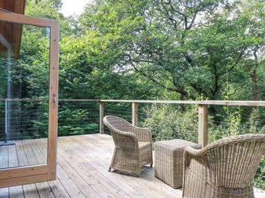 A wooden deck with two wicker chairs and a wicker table surrounded by trees at 4 Stonerush Valley in Lanreath