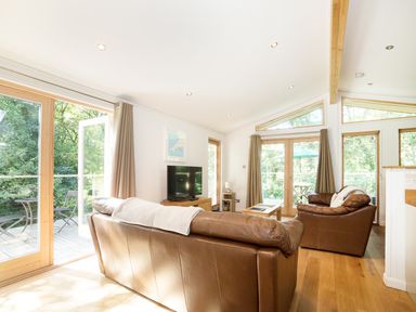 A living room with brown leather sofas a wooden coffee table a television and large windows at 7 Streamside in Lanreath