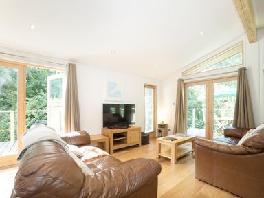 A living room with two brown leather sofas a wooden coffee table and a TV on a wooden stand at 7 Streamside in Lanreath