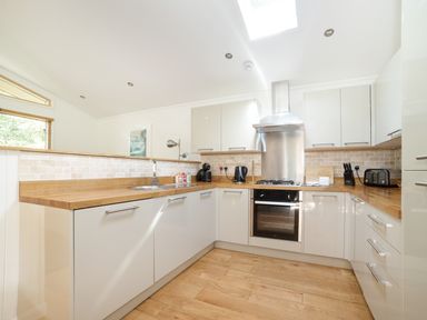 A kitchen with wooden countertops white cabinets a gas stove sink and kitchen appliances at 7 Streamside in Lanreath