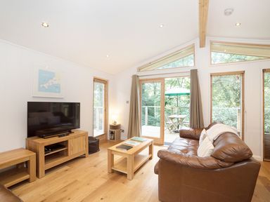 A living room with leather sofa wooden furniture and large windows overlooking a deck at 7 Streamside in Lanreath